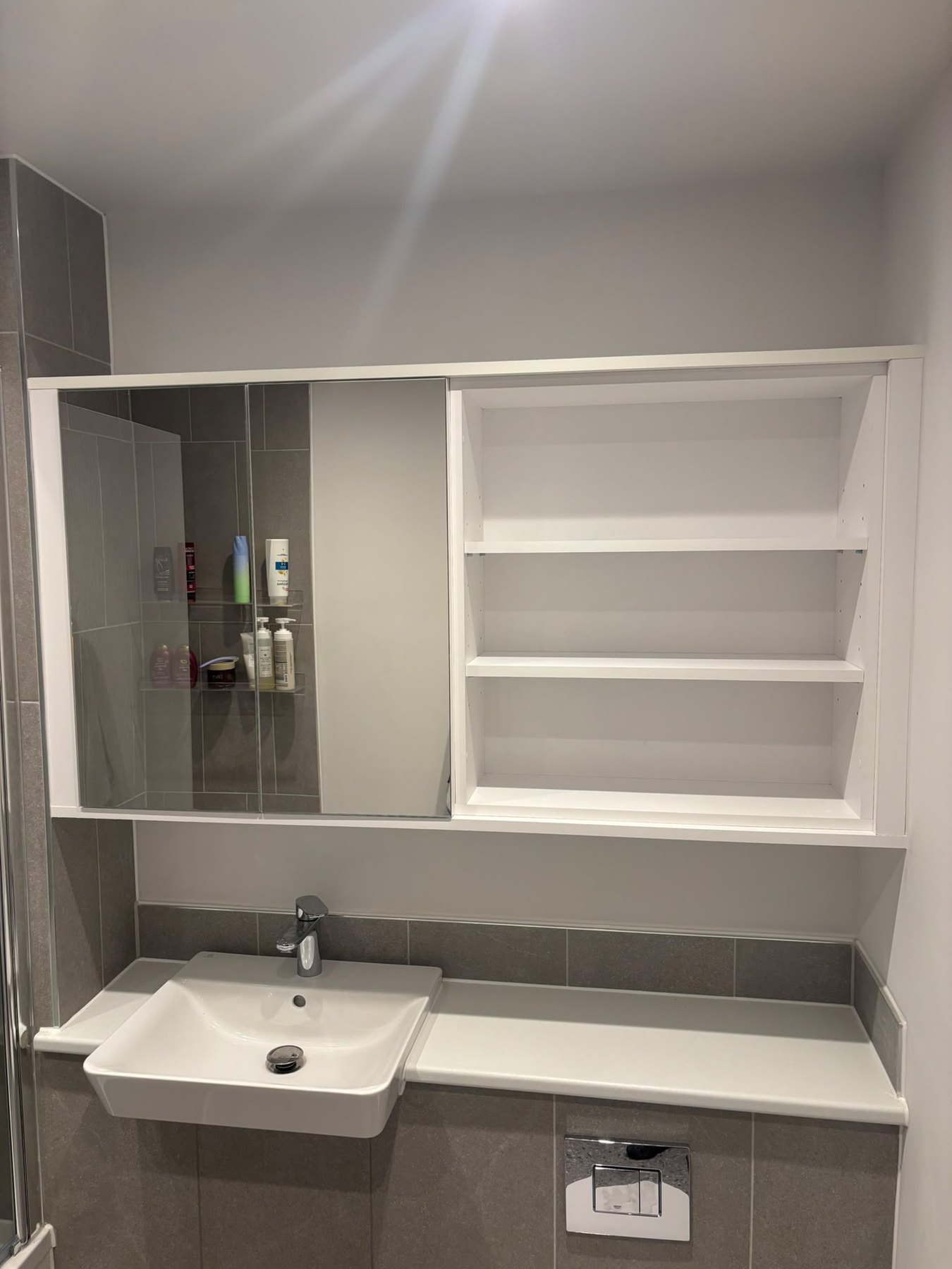 Fitted bathroom unit with a mirrored cabinet over the basin and open shelving alongside