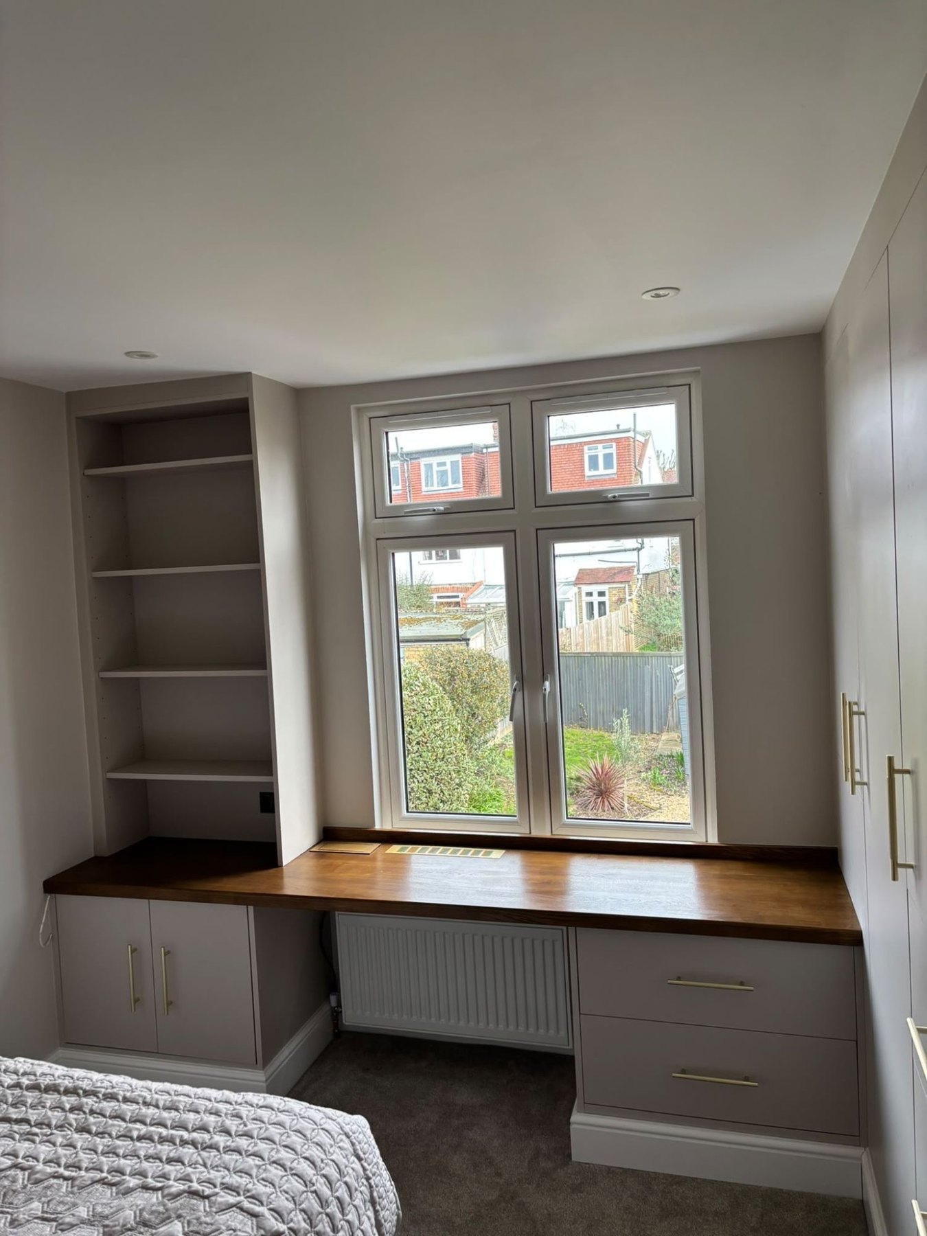 Solid oak desk top fitted under a bedroom window with painted cupboards and drawers below and built-in alcove shelving alongside, Ealing