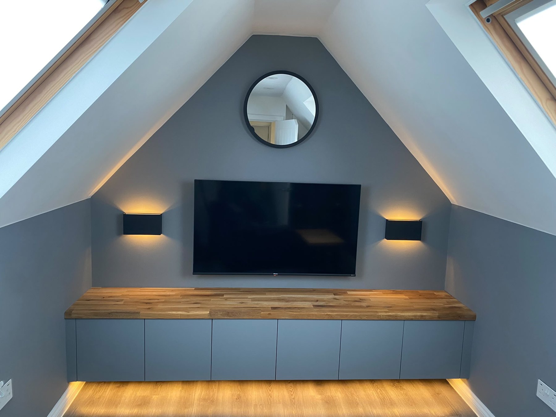 Fitted media unit built into a sloping loft eaves wall, with an oak worktop, integrated lighting and cupboards under the slope