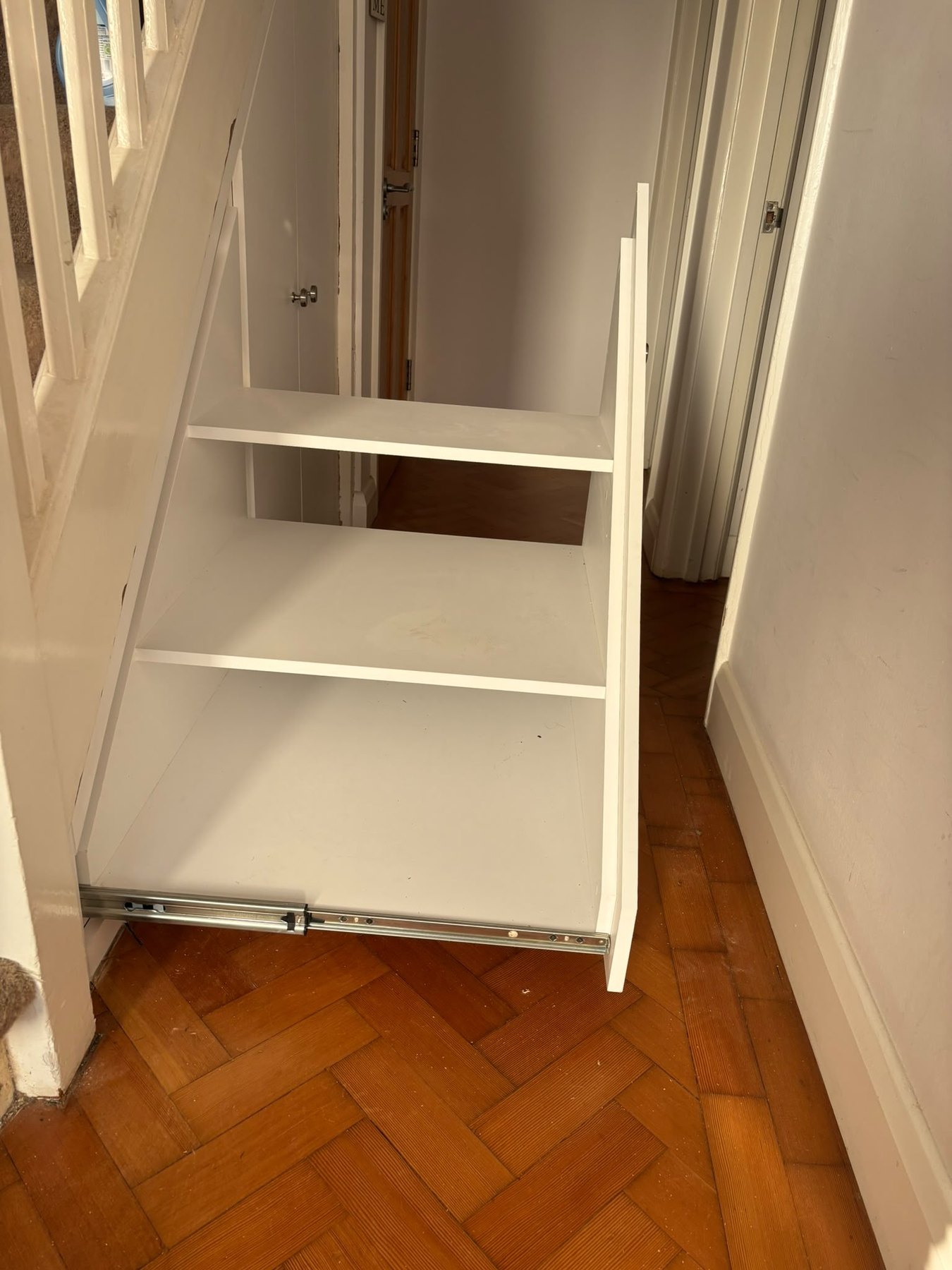 Understairs storage with a full-height pull-out shelving unit drawn out to show the shelves inside