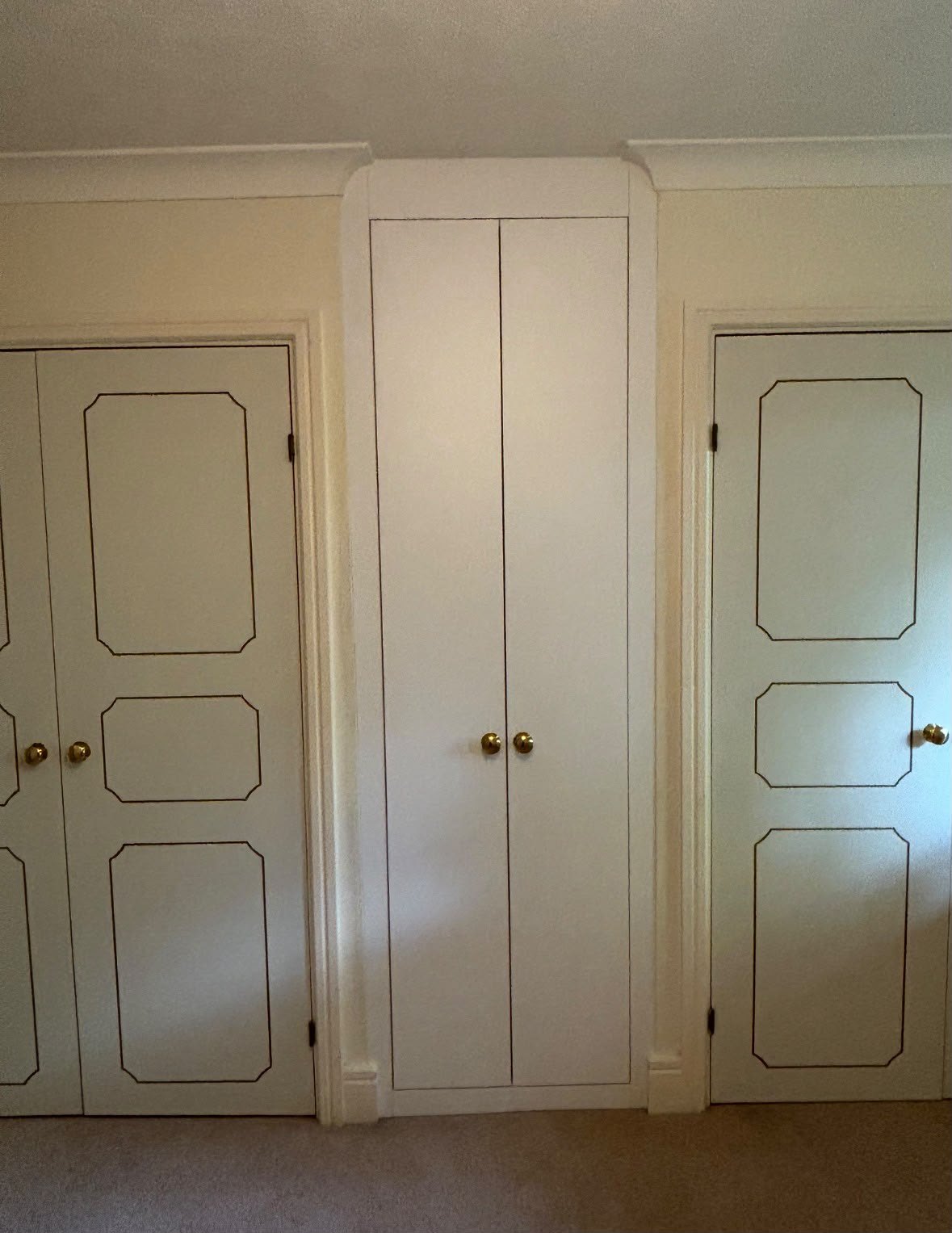 Narrow painted wardrobe built into the gap between two existing units and matched to their panelled doors and brass knobs, Chalfont