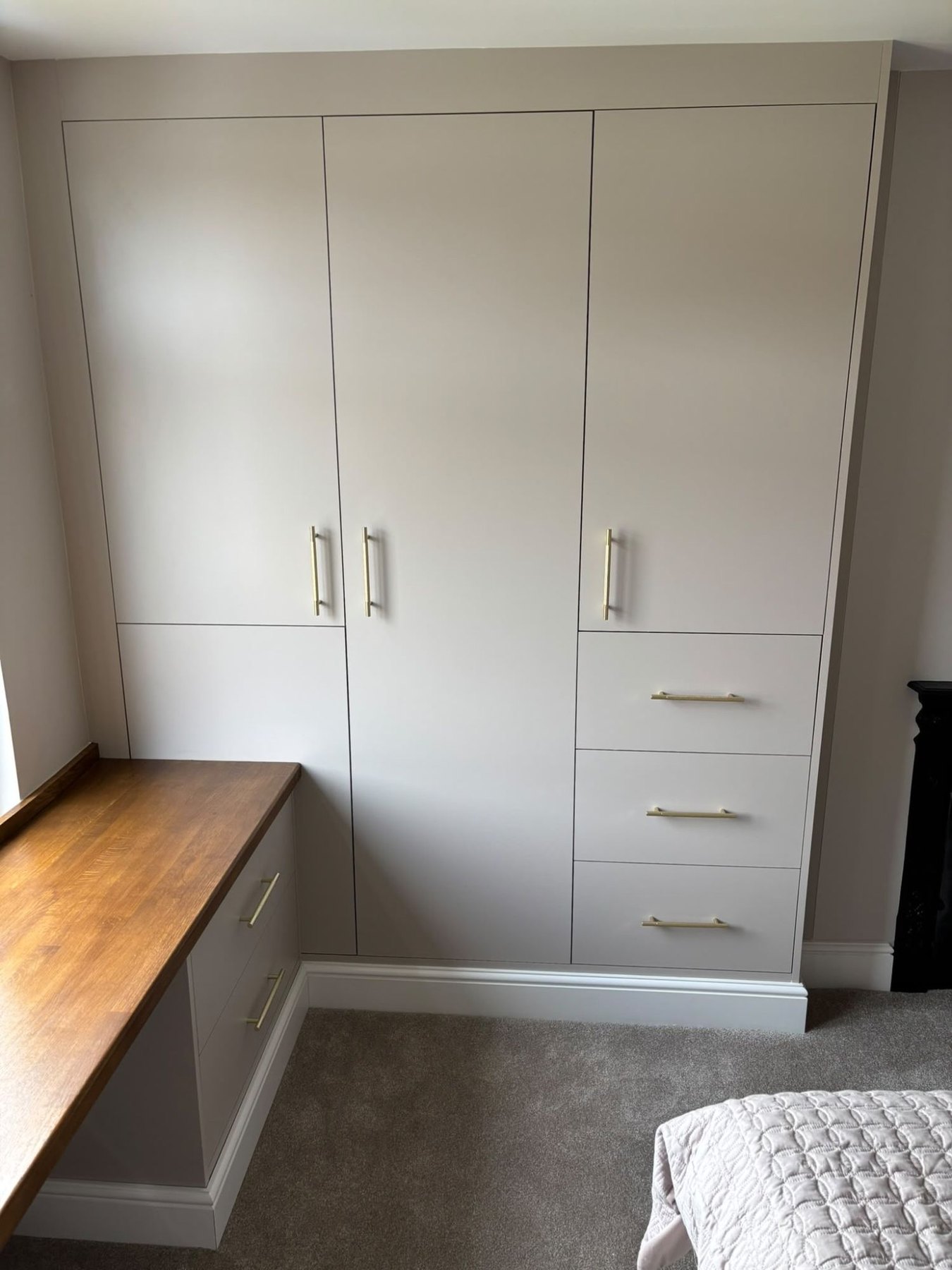 Painted fitted wardrobe with three doors, drawers and brass handles, built floor to ceiling beside a chimney breast with a solid oak desk top running into it, Ealing